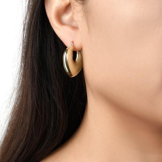 Model photo of chunky gold hoop earrings in the shape of a heart, these silver earrings are elegant and perfect for every day